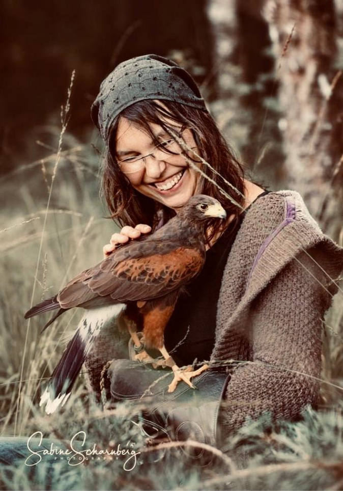Lächelnde Frau sitzt im Grass mit Falken auf der Hand