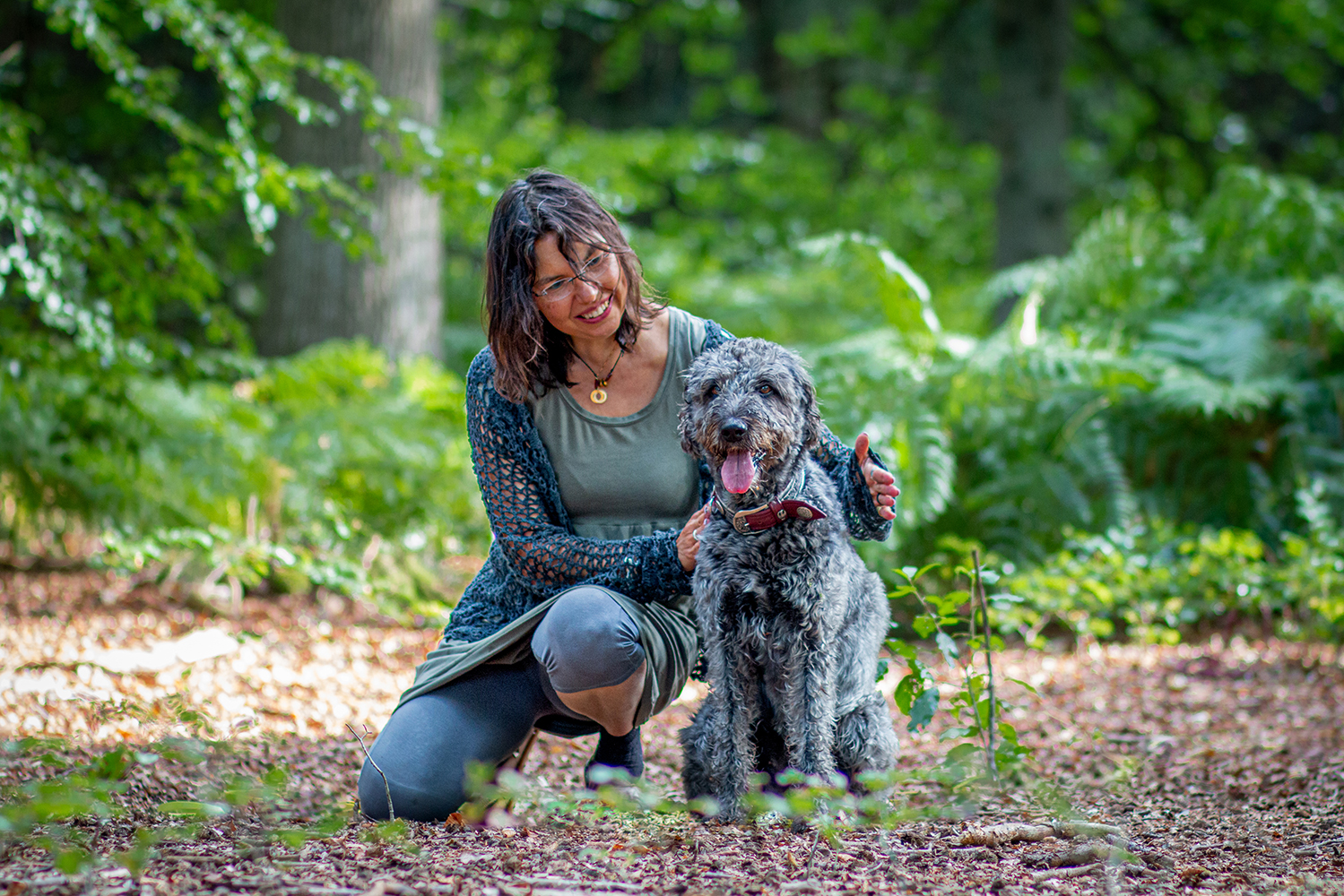 Frau mit Arme um einen sitzenden Hund im Wald